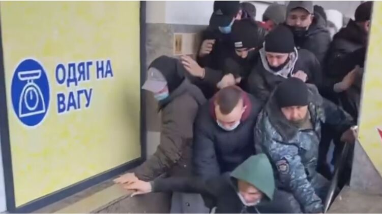 Охранник магазина держался за перила, чтобы его не снесли покупатели. Скриншот с видео